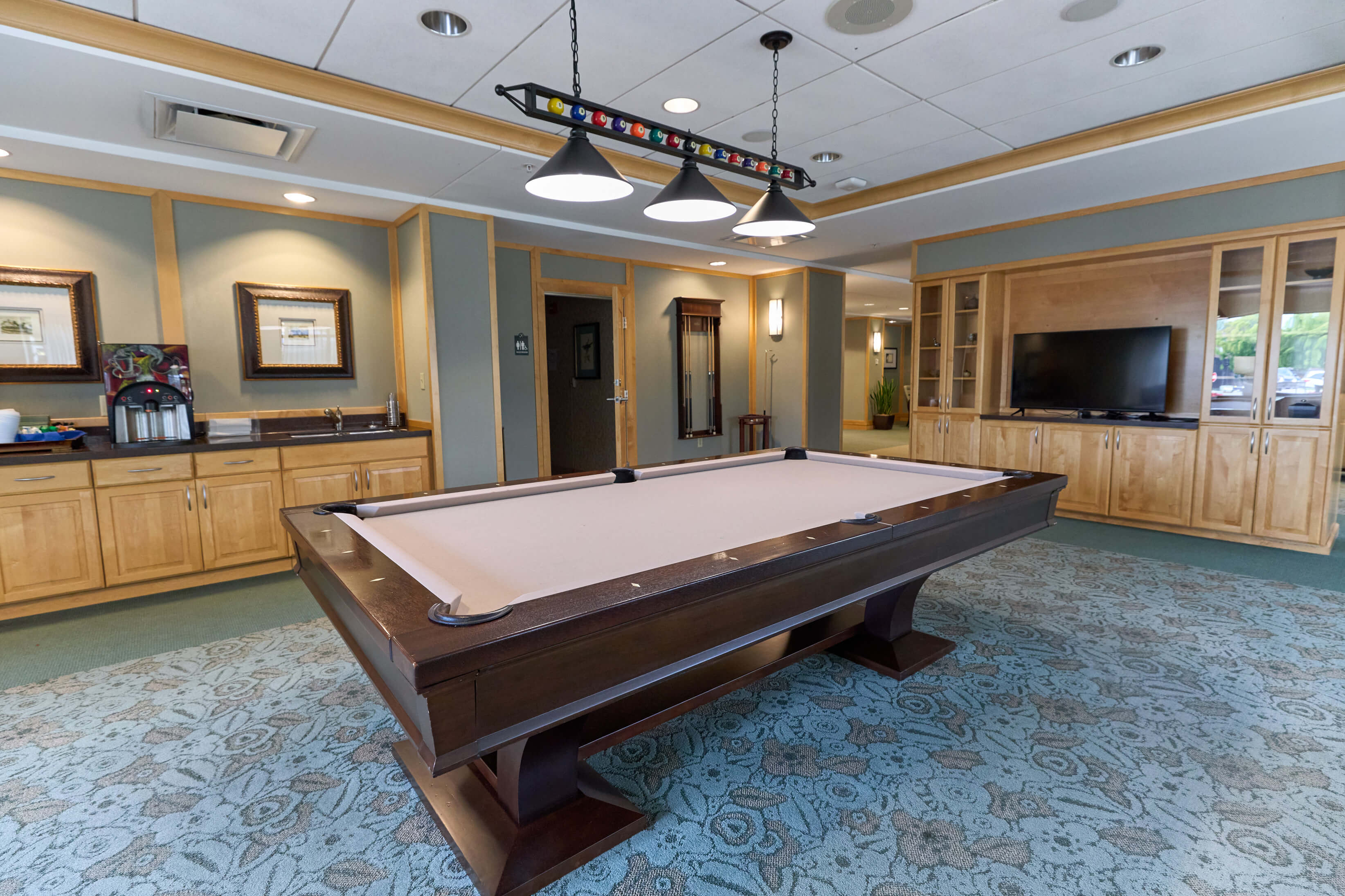 Well-lit billiards room with a pool table, wooden cabinets, TV, and lounge seating area.