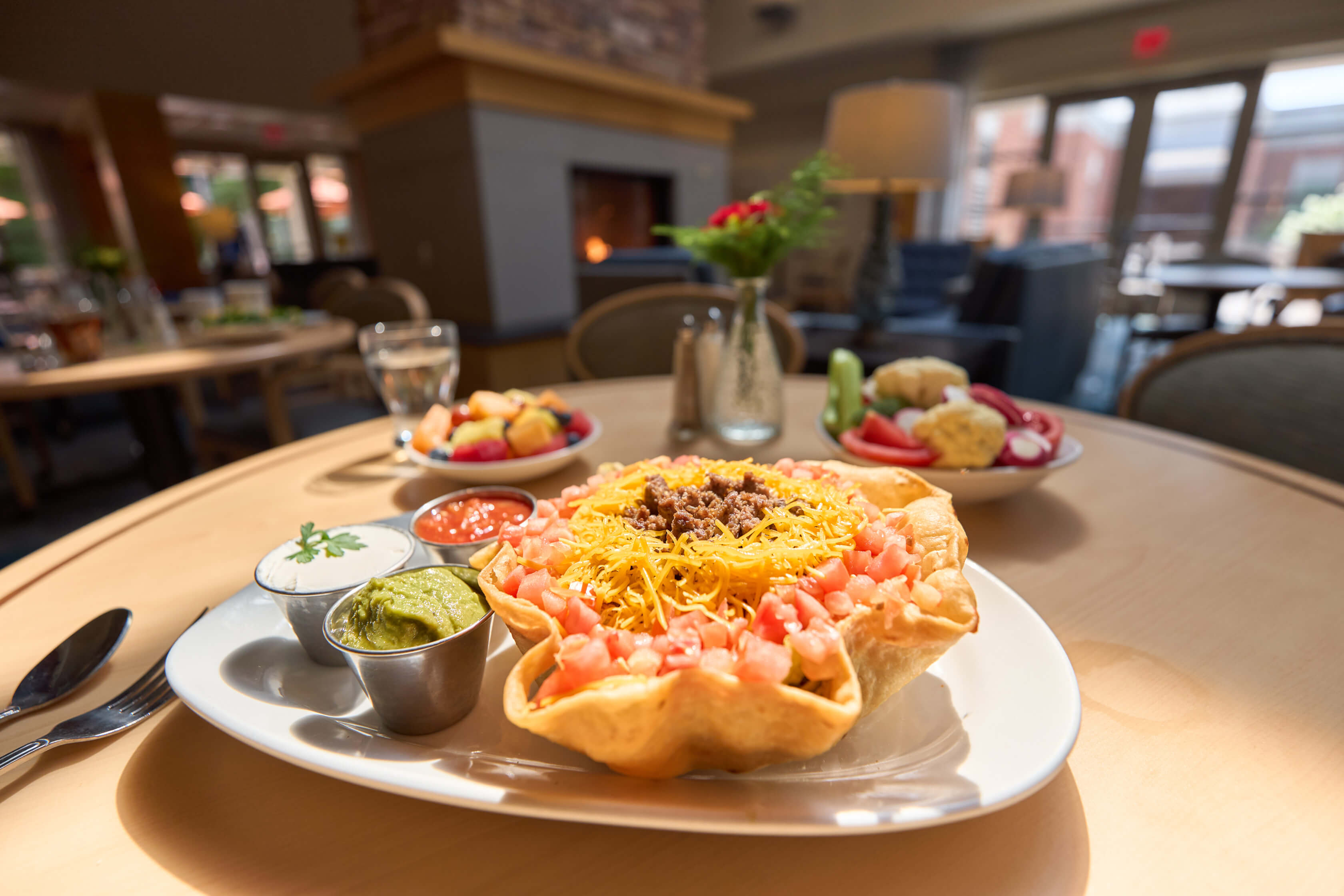 Delicious taco salad with salsa, guacamole, and sour cream in a cozy dining area near a fireplace.