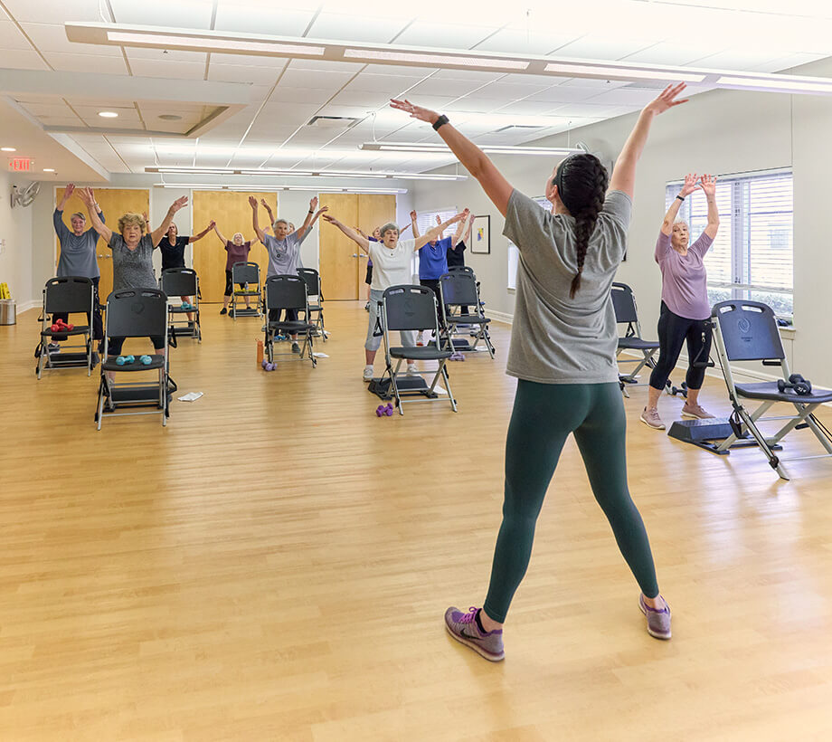 Instructor leading seniors in an exercise in a bright spacious room with wooden flooring