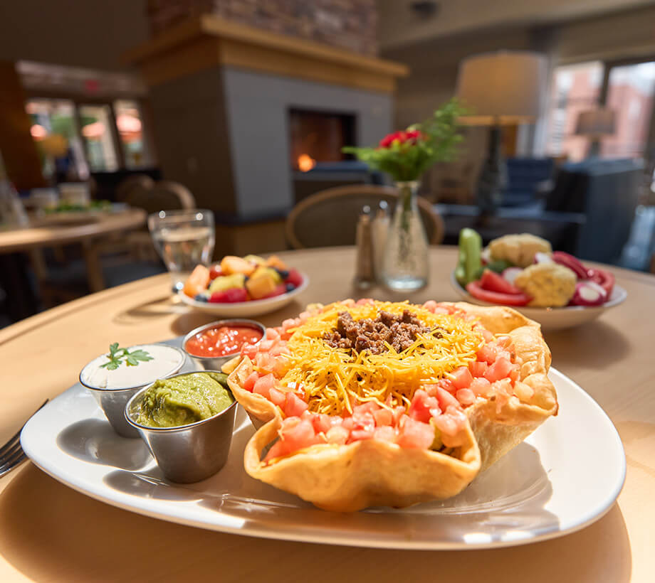 Close-up of taco salad with sour cream, guacamole, and salsa in a senior living dining area.