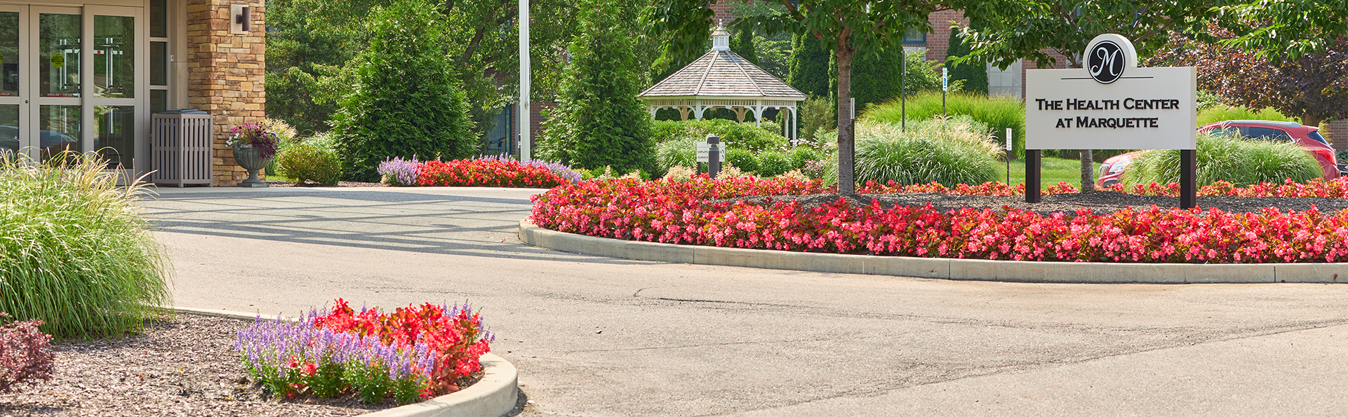 Main entrance to health center with a modern canopy, surrounded by trees and vibrant flowers.
