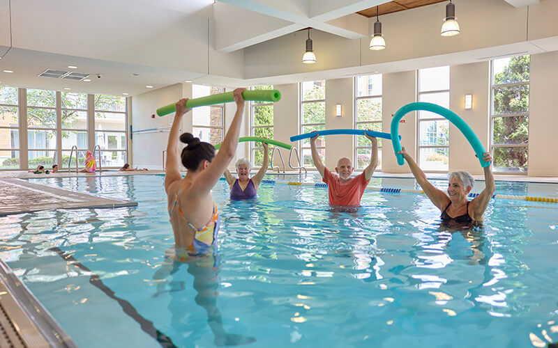 Residents enjoying a water aerobics in indoor pool at a senior living community.