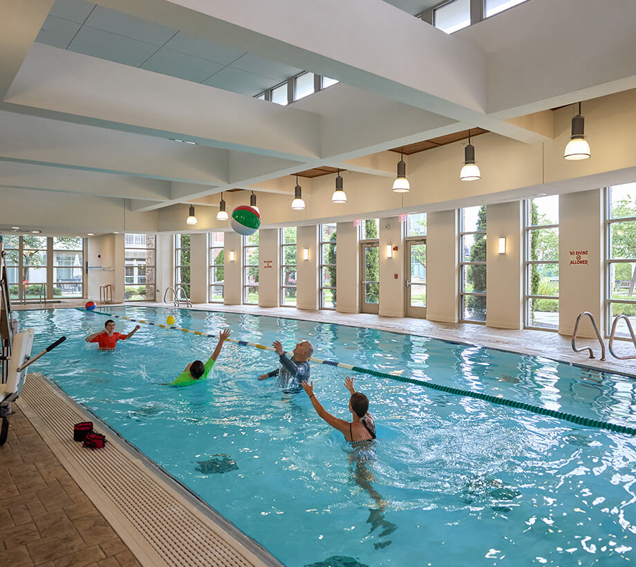 Residents enjoying a game with a beach ball in an indoor swimming pool at a senior living community.