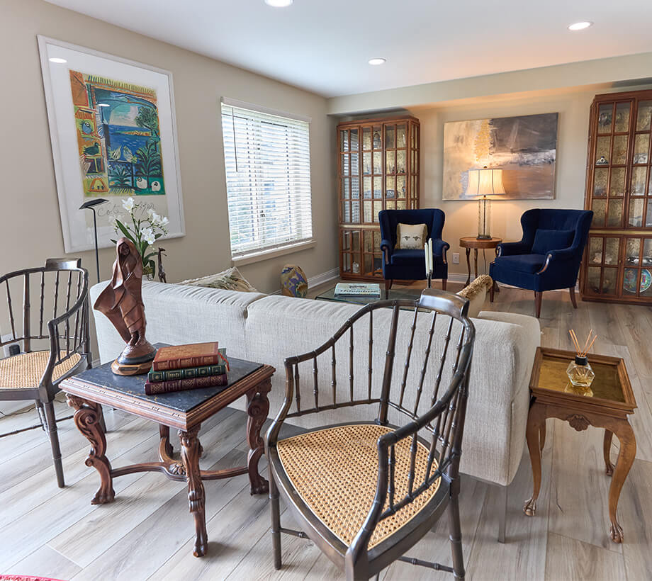Cozy living area with white sofa, wooden chairs, books, and two blue armchairs near a window.