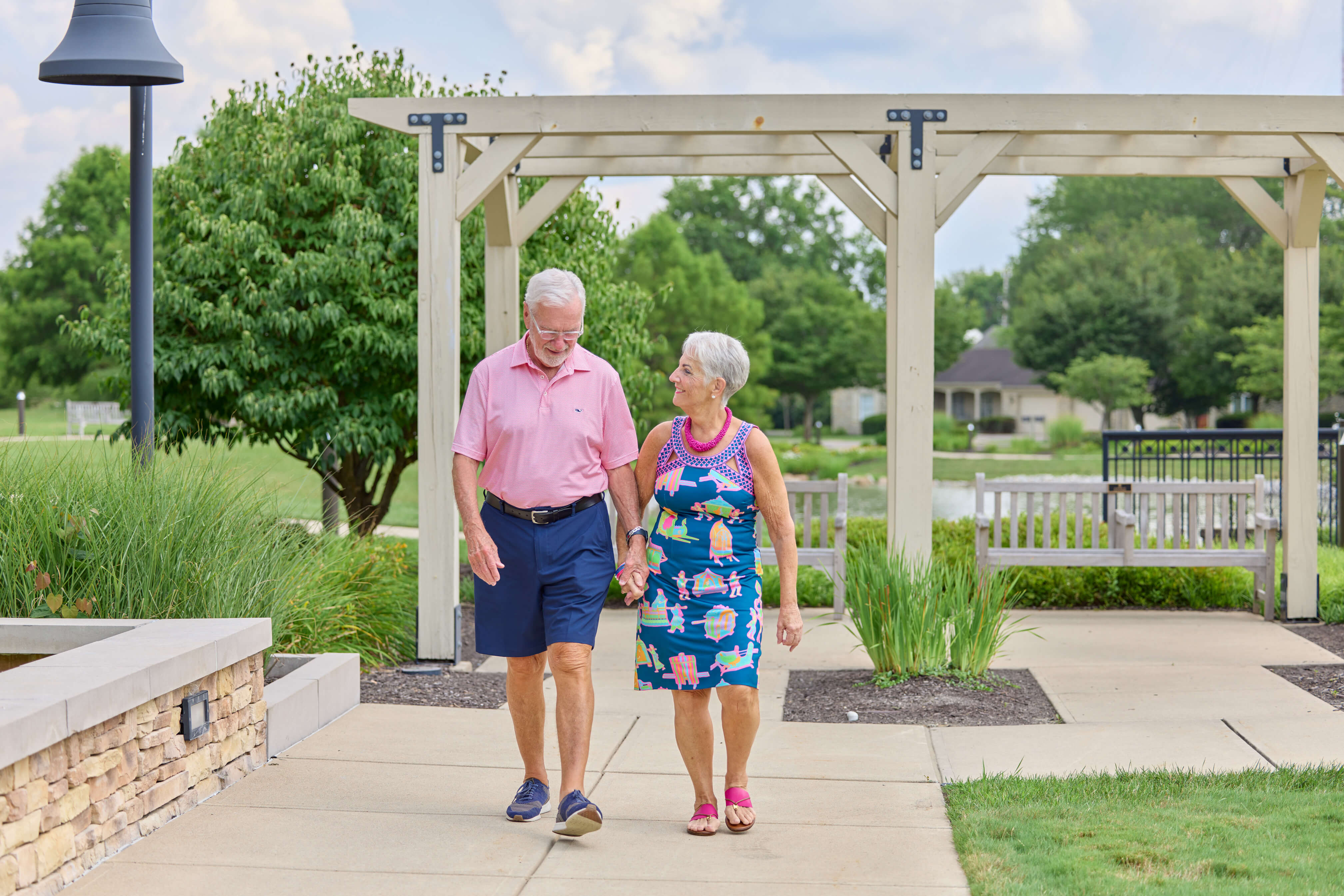 A couple walks hand-in-hand in the courtyard of a senior living community.