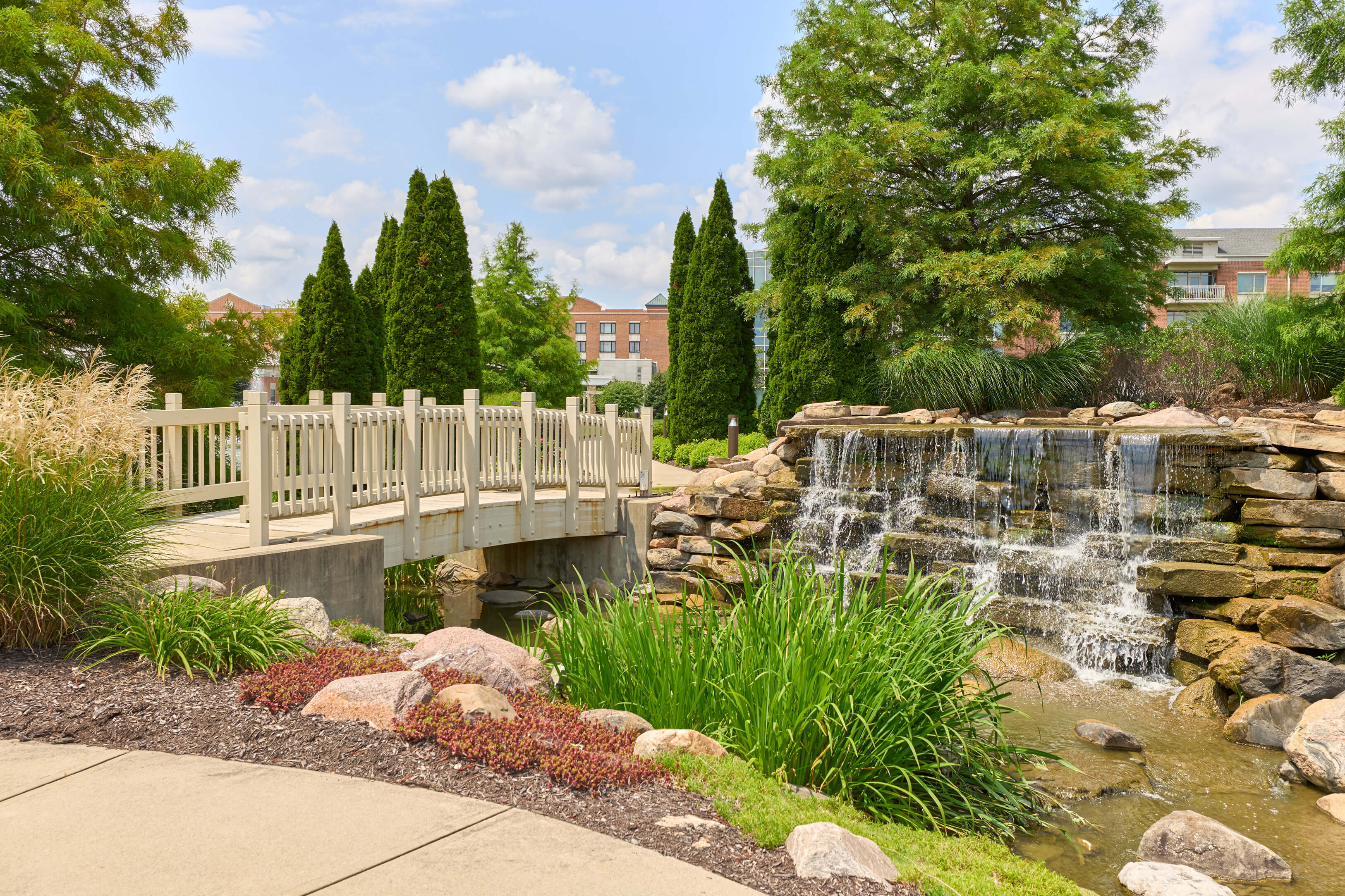 Scenic view of a garden with a wooden bridge and waterfall near residential units.
