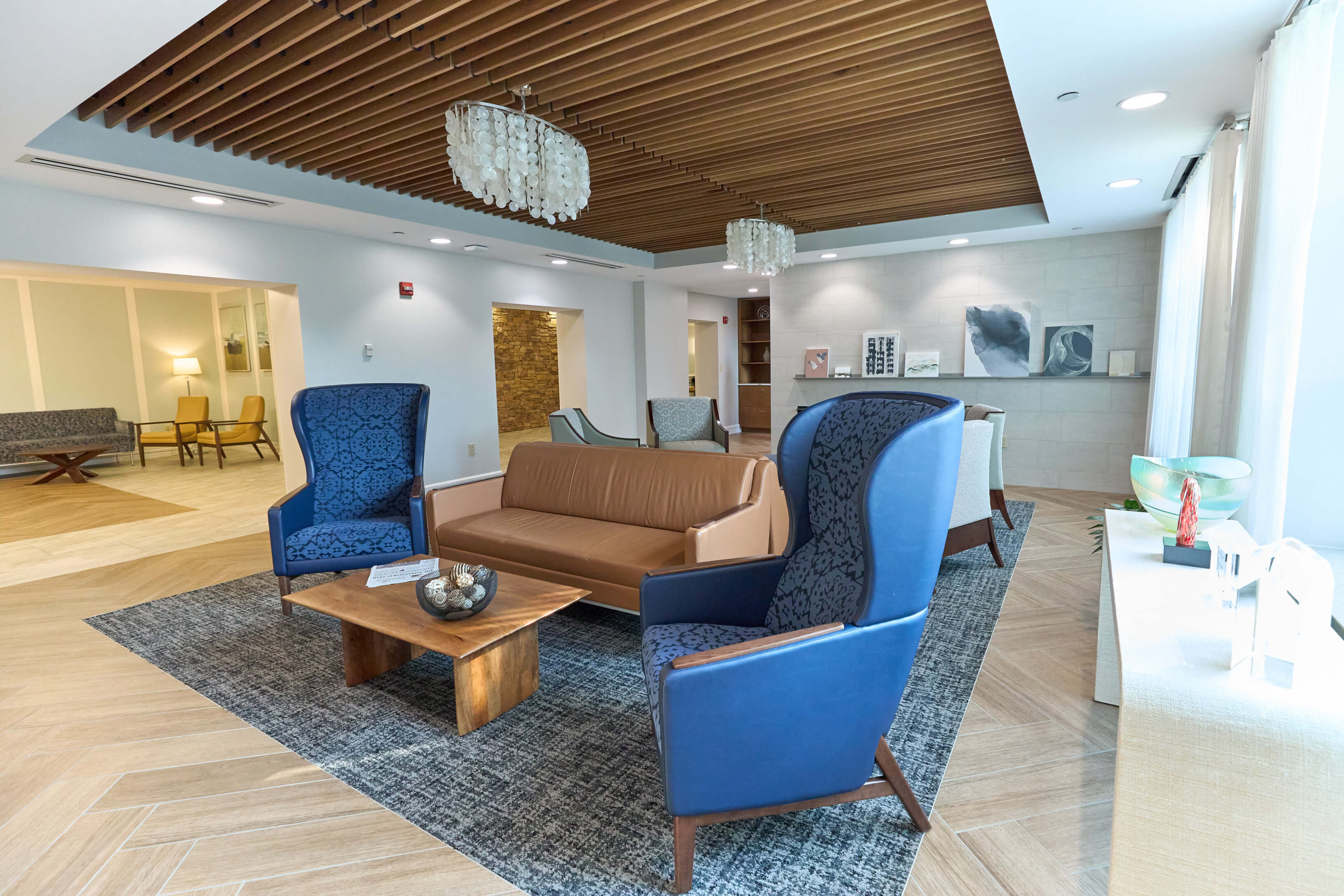 Modern seating area in main room with blue chairs, leather sofa, and a wooden coffee table.
