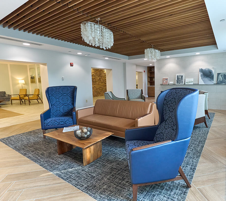 Modern community room with blue armchairs, tan leather sofa, wooden coffee table, and chandelier.