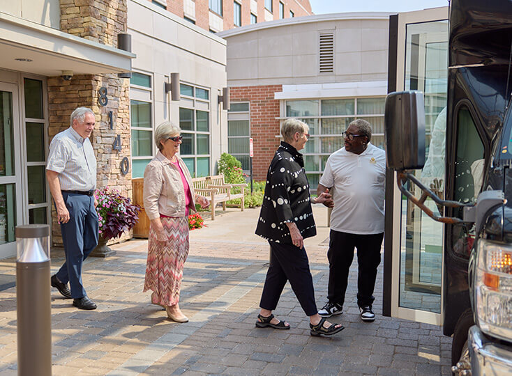Residents of a senior living community boarding a shuttle bus outside the main building.