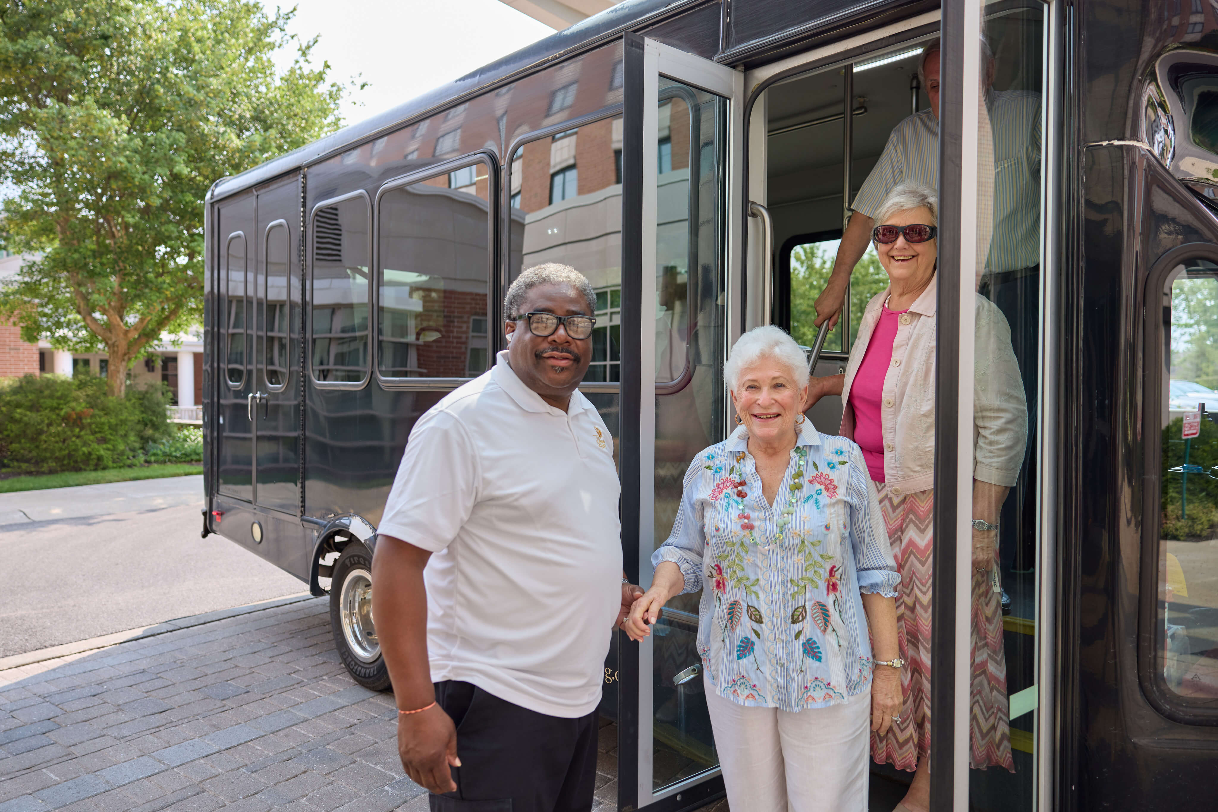 Residents of a senior living community stepping off a shuttle bus with assistance.