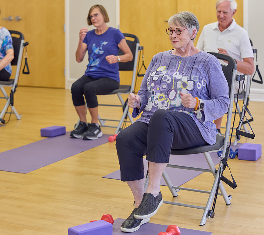 Group of seniors participating in a seated exercise in a living community.
