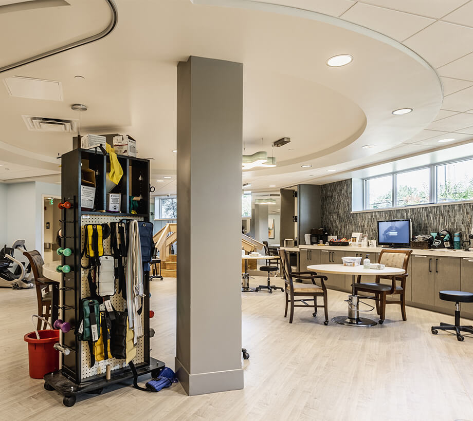 Well-lit room in a senior living community with exercise equipment, tables, and chairs.
