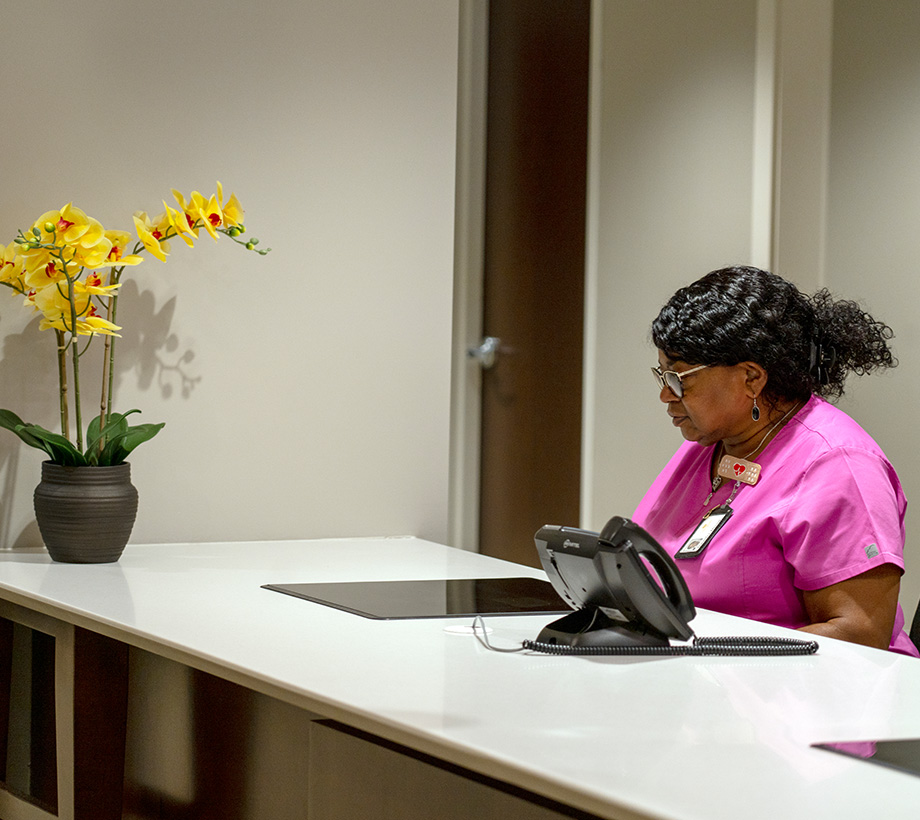 Receptionist in pink uniform attending to residents at the front desk of a senior living community.