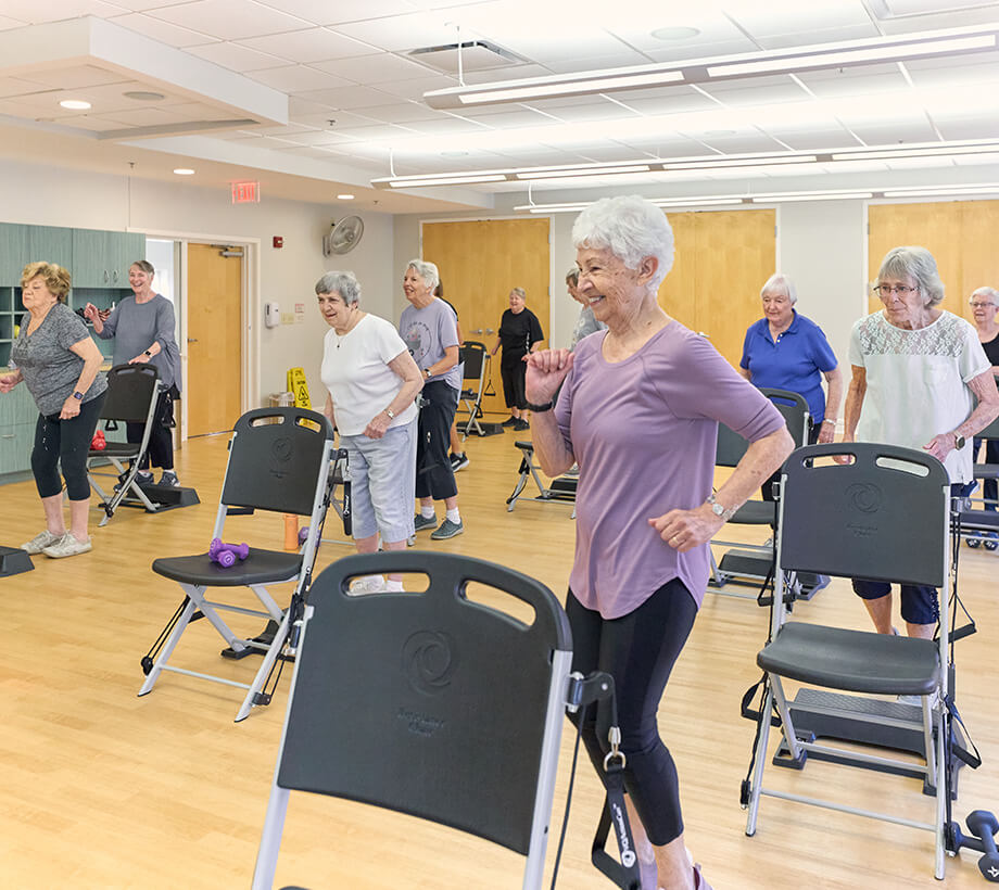 Senior adults engaging in a chair exercise in a well-lit community room.