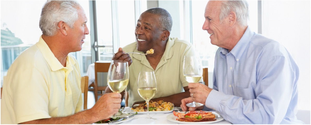 Three senior men enjoy a meal around dinner table