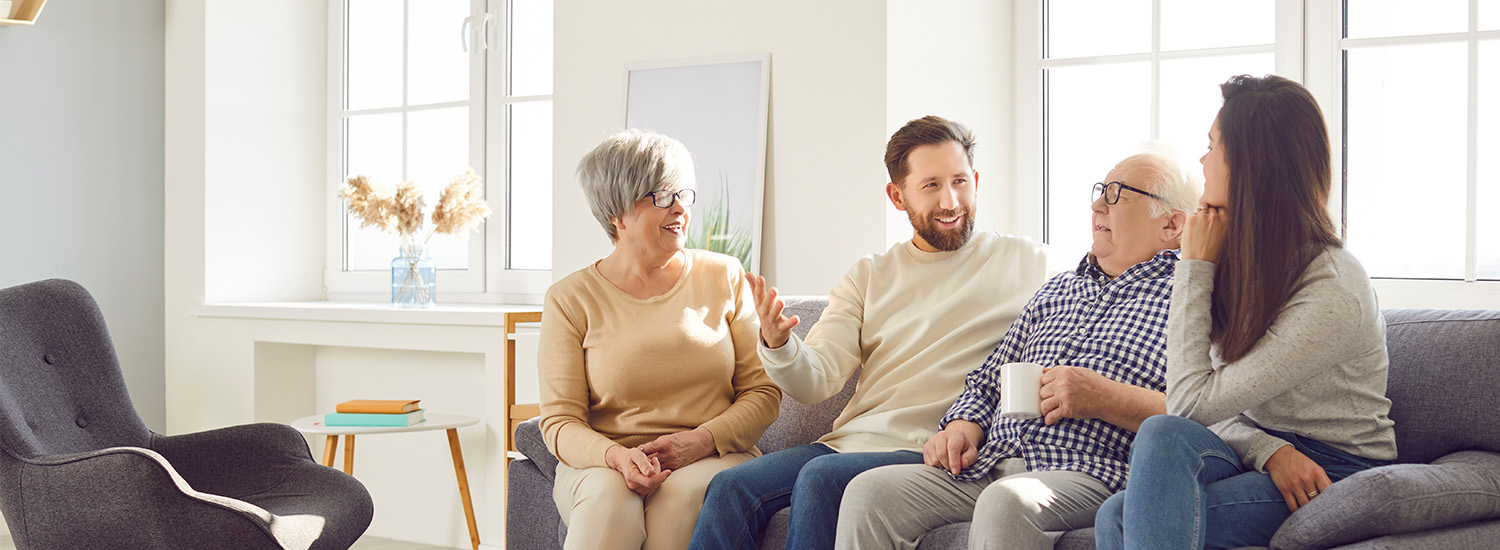 Four family members sit on the couch and smile while having a discussion