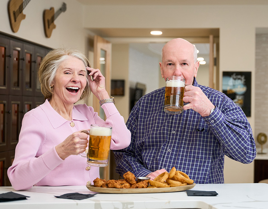 Senior couple smiling as they enjoy beers and plate of wings