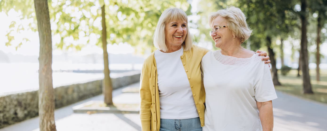Two senior women walking down a path and laughing
