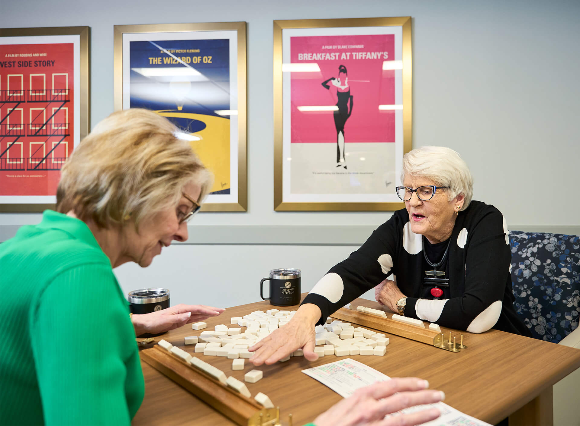 Two women enjoying a tabletop game in a cozy community room with art on the walls.
