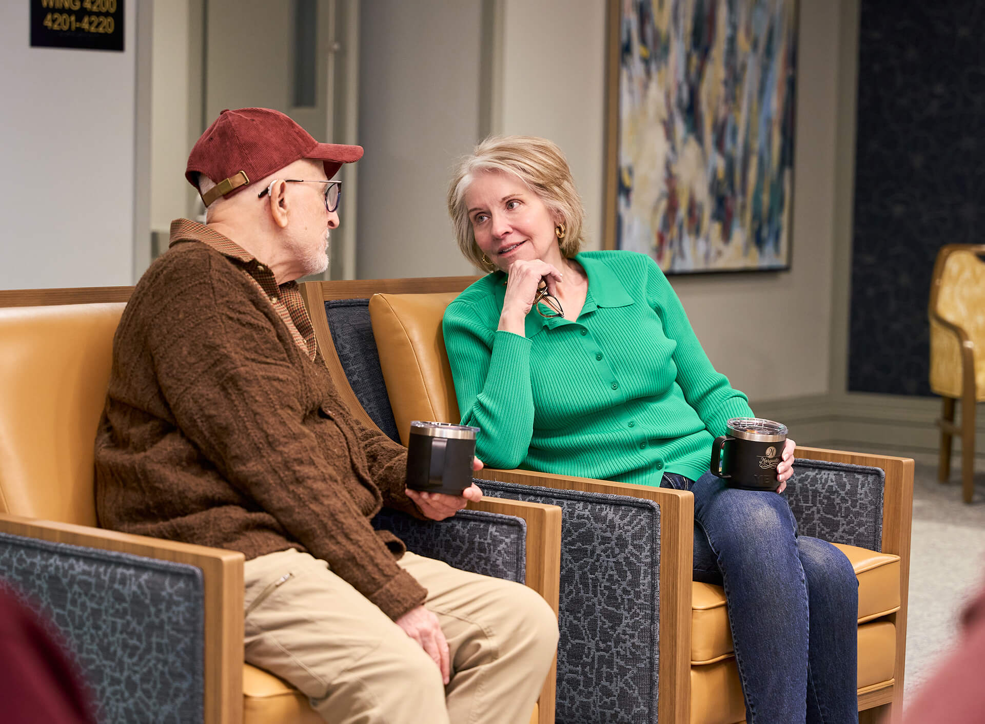 Two seniors enjoying coffee and conversation in a community lounge area.