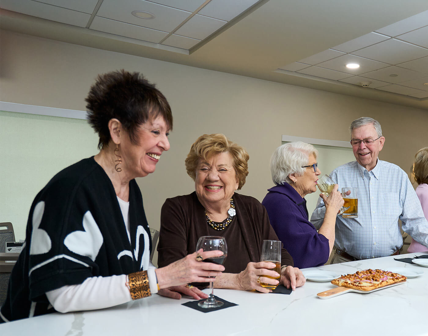 Group of seniors laughing and enjoying drinks at a bar counter.