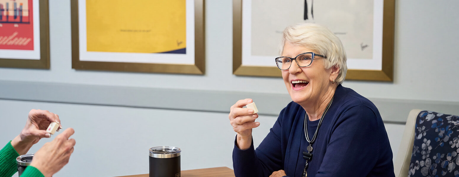 Elderly woman with glasses enjoying a game in a communal area.